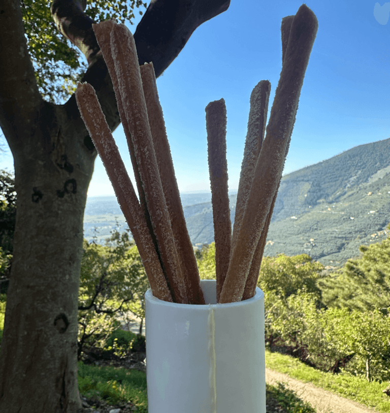 Grissini fatti in casa in un vaso bianco, con la valle di Calci sullo sfondo.